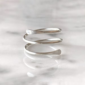 May include: A silver ring with a triple spiral design. The ring is made of a single piece of metal that is twisted into a spiral shape.