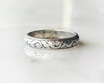 May include: A silver band ring with a delicate floral design. The ring is simple and elegant, perfect for everyday wear.