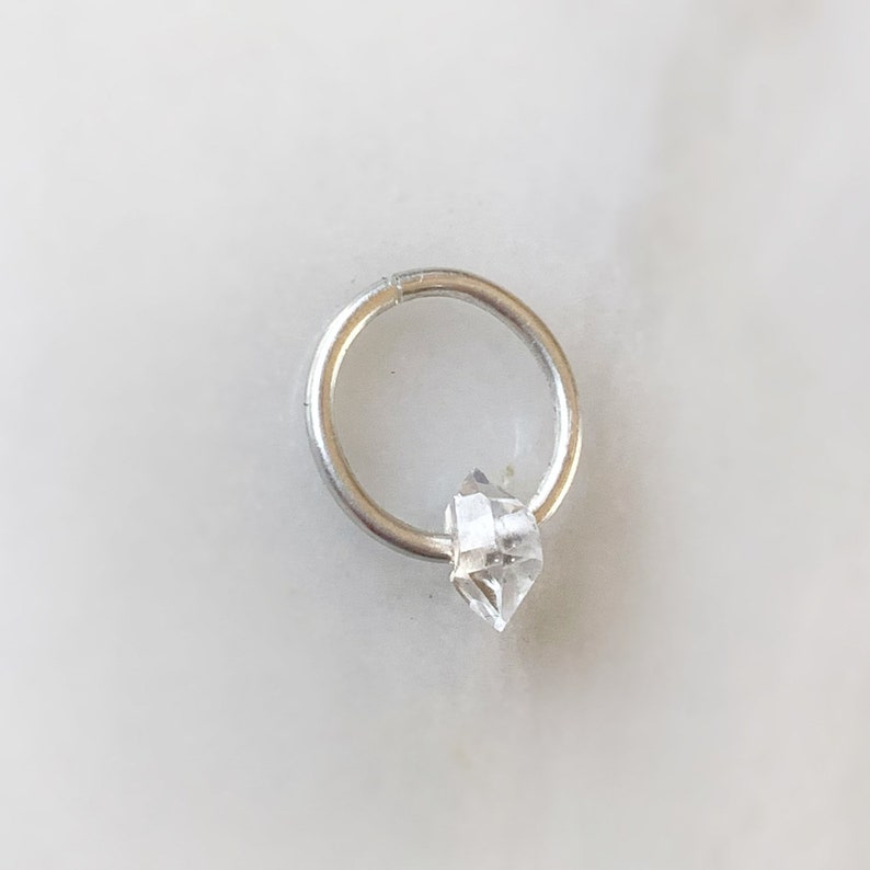 Op de afbeelding: Een zilveren oorring met een hanger van helder kwartskristal.
