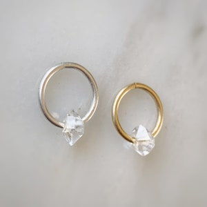 Op de afbeelding: Twee creolen, een zilveren en een gouden, elk met een helder diamantvormig kristal dat eraan hangt.