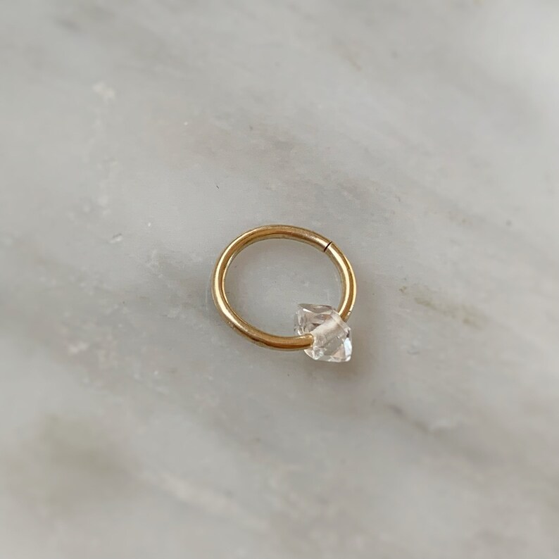 Op de afbeelding: Een gouden oorring met een heldere, gefacetteerde edelsteen. De oorring is een populaire keuze voor kraakbeenpiercings.