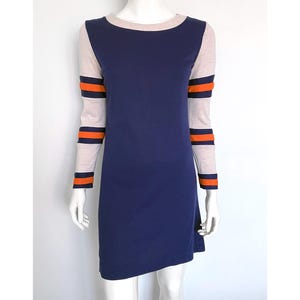 Pode incluir: Um vestido azul marinho com decote e mangas bege. As mangas apresentam listras laranja e azul marinho. O vestido é exibido em um manequim sobre um fundo branco.