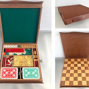 Pode incluir: Uma caixa de jogos de madeira com um interior de feltro verde. A caixa contém uma variedade de jogos, incluindo dominó, dados, cartas de jogo e um tabuleiro de xadrez. A caixa está fechada na primeira imagem e aberta na segunda imagem, revelando o conteúdo.