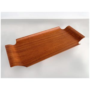 Puede incluir: Una bandeja rectangular de madera para servir con un borde curvo y elevado y asas recortadas. La bandeja tiene un color marrón rojizo intenso y un patrón de vetas de madera visible. Diseñada para servir alimentos o exhibir artículos.