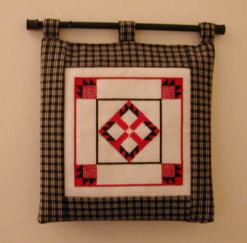 May include: A black and white checkered fabric wall hanging with a red and black geometric design in the center.