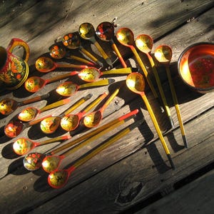 May include: A collection of wooden kitchenware featuring a pitcher, a bowl, and numerous spoons, all decorated with traditional red, yellow, and black floral patterns. The items have a glossy finish and are arranged on a wooden surface.