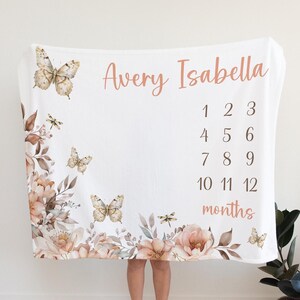 Puede incluir: Una manta blanca para hitos de beb&eacute; con un dise&ntilde;o floral con mariposas y lib&eacute;lulas. La manta tiene los nombres "Avery Isabella" y los n&uacute;meros del 1 al 12 para cada mes del a&ntilde;o.