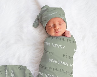 May include: A sage green swaddle blanket with the names "Benjamin" and "Henry" repeated in white text. A baby is swaddled in the blanket and wearing a matching sage green hat with the same text.