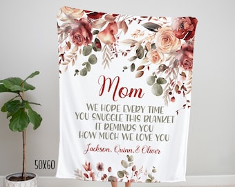 May include: A white fleece blanket with a floral design in shades of red, pink, and green. The blanket has a personalized message that reads "Mom, We hope every time you snuggle this blanket it reminds you how much we love you, Jackson, Quinn, & Oliver."