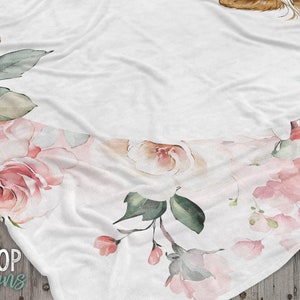 May include: A white blanket with a floral design featuring pink roses and green leaves. The blanket has a soft, fuzzy texture and is perfect for cuddling up on the couch.