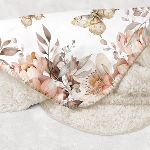 Puede incluir: Una suave manta de sherpa blanca con un estampado floral que presenta delicadas mariposas y flores rosa claro. La manta es perfecta para agregar un toque de elegancia y calidez a cualquier habitaci&oacute;n.