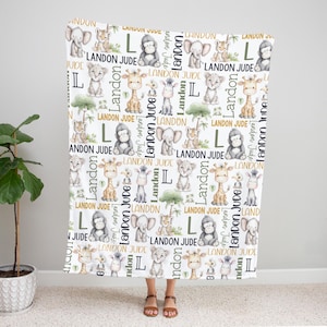 A person is standing in front of a white blanket with a repeating pattern of various animals, including elephants, giraffes, and zebras, along with the name 'Landon' written on it.