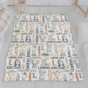 a white and green blanket with a repeating pattern of cartoon animal illustrations, including a giraffe, lion, and elephant, along with the name 'Landon' written in various colors.