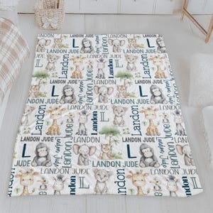a white and blue blanket with a repeating pattern of cartoon animal illustrations, including giraffes, elephants, and lions, along with the name 'Landon' written in various fonts and sizes.