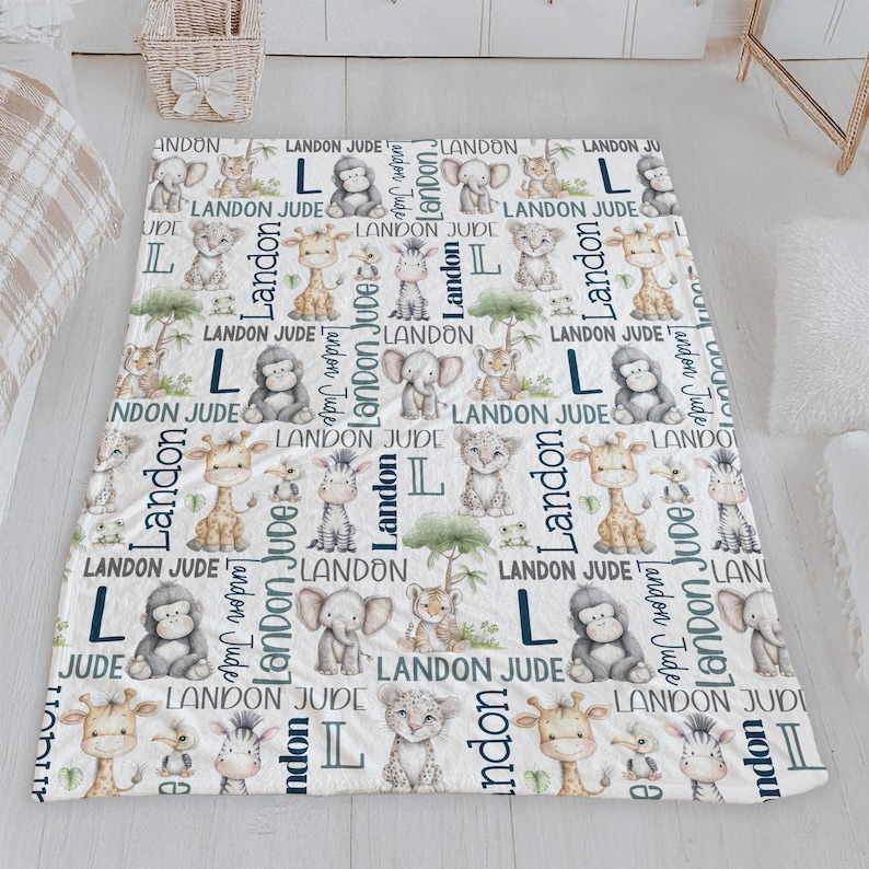a white and blue blanket with a repeating pattern of cartoon animal illustrations, including giraffes, elephants, and lions, along with the name 'Landon' written in various fonts and sizes.