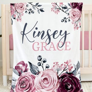 May include: A white rectangular blanket featuring a watercolor floral design in shades of dusty rose, burgundy, and dark gray. The text Kinsey GRACE is printed in the center in a combination of dark gray script and pink block lettering.