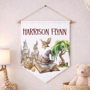 May include: A white fabric wall banner featuring the name HARRISON FLYNN in dark red text. The illustration includes a large castle, a flying owl carrying a letter, a pointed wizard hat resting on an open book, a willow tree, and luggage.