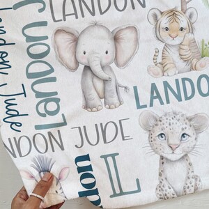 a hand holding a towel with various animal illustrations, including an elephant, a tiger, and a leopard, along with the names 'LANDON' and 'JUDGE' written on it.