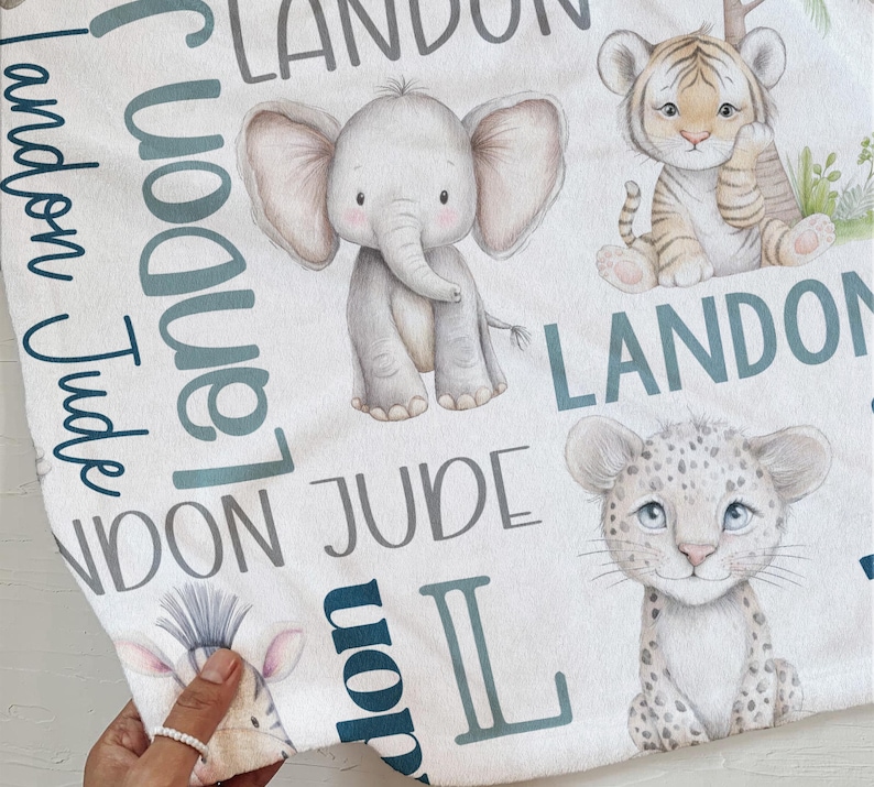 a hand holding a towel with various animal illustrations, including an elephant, a tiger, and a leopard, along with the names 'LANDON' and 'JUDGE' written on it.