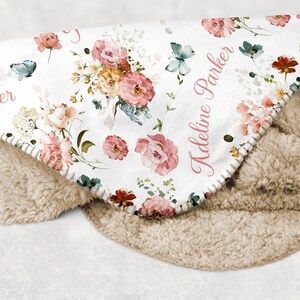 Pode incluir: Um cobertor branco com um design floral com rosas rosa e p&ecirc;ssego, borboletas azuis e folhas verdes. O cobertor tem um forro de sherpa bege macio e os nomes "Parker" e "Adeline Parker" s&atilde;o impressos.