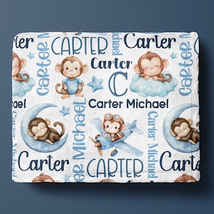 May include: A white baby blanket featuring a repeating pattern of cartoon monkeys, clouds, stars, and the name "Carter" in blue. The blanket shows a monkey in a plane, on a cloud, and on a crescent moon.