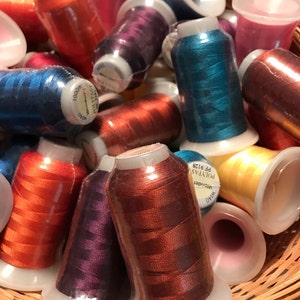May include: A basket filled with spools of colorful embroidery thread. The spools are labeled "Wonder" and "Poly-Fast" and have a white background with black text. The spools are in various colors, including red, orange, yellow, green, blue, purple, and pink.