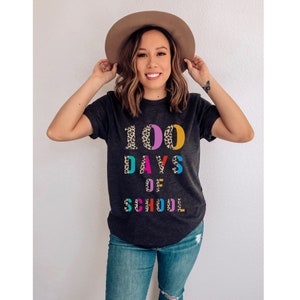 Peut inclure: Un t-shirt noir avec un motif l&eacute;opard qui dit "100 jours d'&eacute;cole" en lettres color&eacute;es.