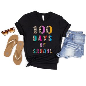Peut inclure: T-shirt noir avec le texte "100 jours d'&eacute;cole" en lettres color&eacute;es avec un motif l&eacute;opard.