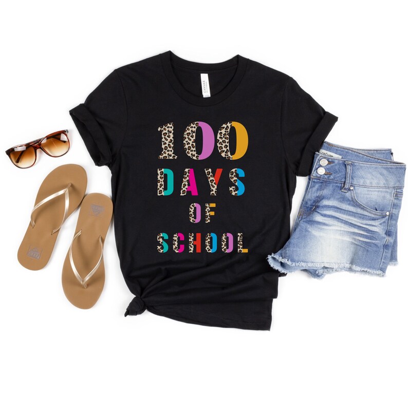 Peut inclure: T-shirt noir avec le texte "100 jours d'&eacute;cole" en lettres color&eacute;es avec un motif l&eacute;opard.