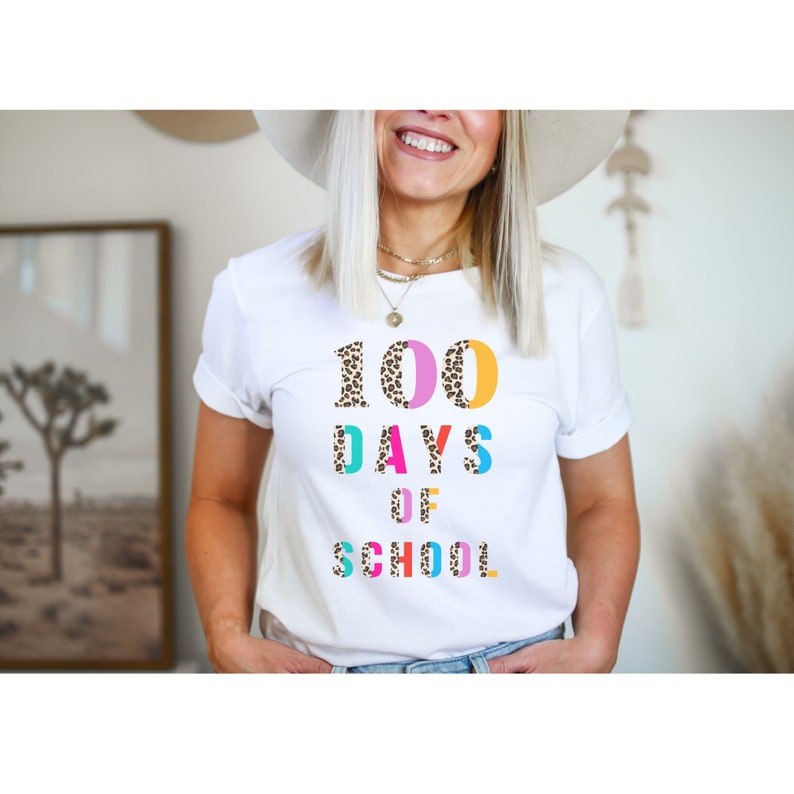 Peut inclure: T-shirt blanc avec le texte "100 DAYS OF SCHOOL" en lettres color&eacute;es avec un motif l&eacute;opard.