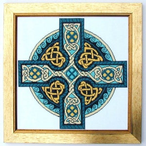 Puede incluir: Una obra de arte en punto de cruz enmarcada con un dise&ntilde;o de cruz celta. La cruz presenta intrincados patrones de nudos en tonos turquesa, dorado y crema. La obra est&aacute; sobre un fondo blanco y enmarcada en un marco de madera dorada.