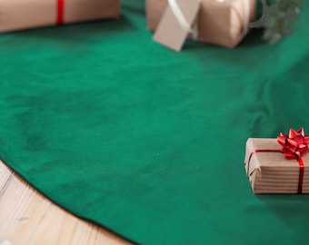 Puede incluir: Una falda de árbol de Navidad de terciopelo verde con regalos envueltos en marrón y un adorno plateado colgando de una rama de árbol de Navidad.