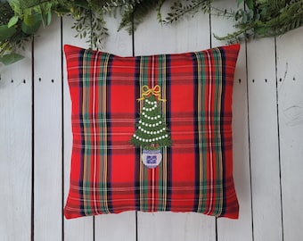 Puede incluir: Cojín de cuadros rojos y verdes con un diseño de árbol de Navidad bordado. El árbol está decorado con cuentas blancas y un lazo amarillo.