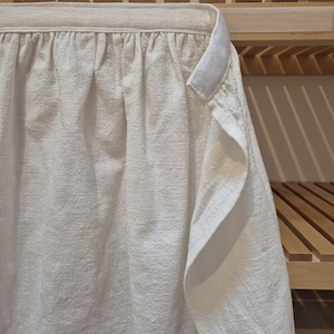 May include: A white long-sleeved shirt with a gathered neckline, hanging on a wooden shelf.