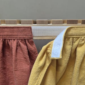 May include: Close-up of two fabric items, one in a warm terracotta colour and the other in a bright yellow. Both have a textured appearance and are gathered at the top. A white velcro strip is visible.