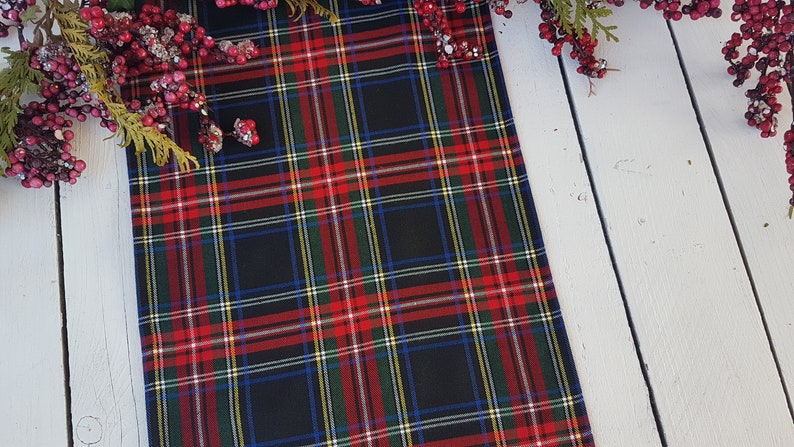 May include: Black and red plaid table runner with a white background. The runner has thin stripes of yellow and blue.