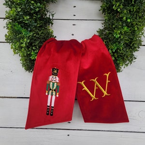 Puede incluir: Calcetín de Navidad de terciopelo rojo con un cascanueces bordado en oro y la letra "W" en el otro lado.