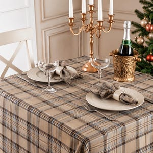 May include: A table set with a beige, brown, and blue plaid tablecloth, two white plates with plaid napkins in rings, two glass coupes, a gold five-arm candelabra with white taper candles, and a bottle in a gold textured ice bucket.