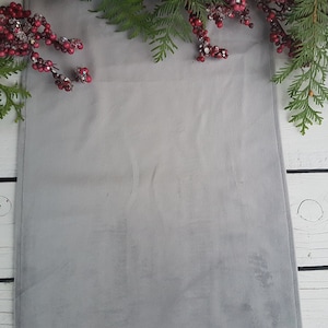May include: A gray table runner with a white background. The table runner is decorated with sprigs of green foliage and red berries.