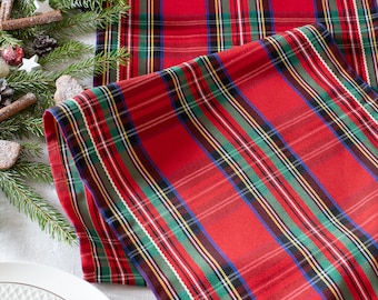 May include: Red and green tartan table runner with white stitching. The runner is folded in half and has a white background.