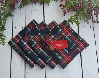 May include: Four red, black, and green plaid napkins with a red ribbon and a small bell. A red tag with the name "Kate" is attached to the ribbon.