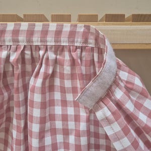 Könnte beinhalten: Rosa-weißes Gingham-Gewebe mit einem weißen Klettverschluss. Der Stoff ist oben gerafft und hat einen gekräuselten Rand.