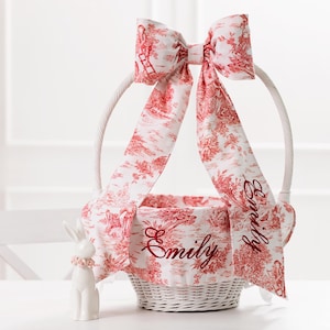 May include: White wicker Easter basket with a red and white toile fabric lining and a large red bow. The basket is decorated with the name "Emily" embroidered in red thread.