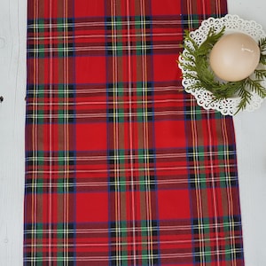 May include: Red and green tartan table runner with a white lace doily and a white candle on top.