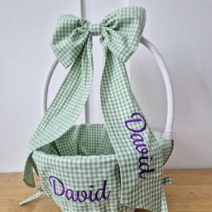 May include: White wicker Easter basket with a green and white gingham bow and matching fabric. The fabric is personalized with the name "David" in purple embroidery.
