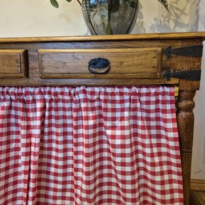 Può includere: Un tavolo console in legno con un cassetto e una tovaglia a quadri rossi e bianchi. Il tavolo ha una finitura in legno scuro e un design semplice.