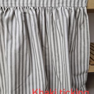 May include: Khaki ticking fabric curtain with vertical stripes in gray and off-white. The curtain is gathered at the top and hangs in soft folds. The text "Khaki ticking" is visible.