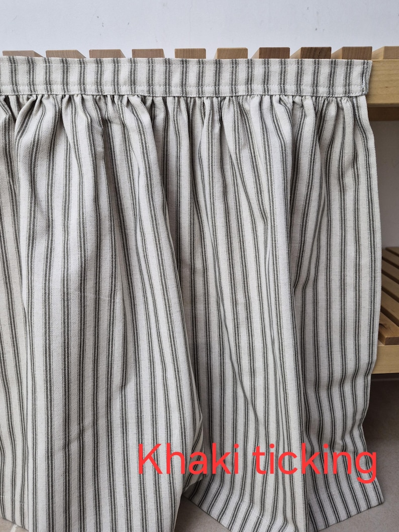 May include: Khaki ticking fabric curtain with vertical stripes in gray and off-white. The curtain is gathered at the top and hangs in soft folds. The text "Khaki ticking" is visible.
