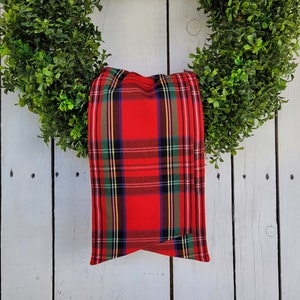 May include: A red and green plaid bow tied around a green wreath. The wreath is hanging on a white wooden door.