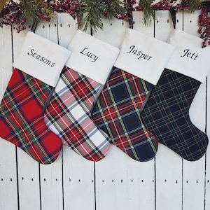 Puede incluir: Cuatro calcetines de Navidad con puños de fieltro blanco y patrones de cuadros. Los calcetines están personalizados con los nombres "Seasons", "Lucy", "Jasper" y "Jett".